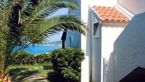 Ein Weg führt zu einem weißen Gebäude mit roten Ziegeldach, umgeben von Grün und mit Blick auf ein Gewässer.