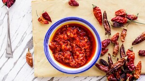 Eine Schüssel rote Soße mit umhergestreuten getrockneten roten Chilischoten auf einer Marmorplatte.