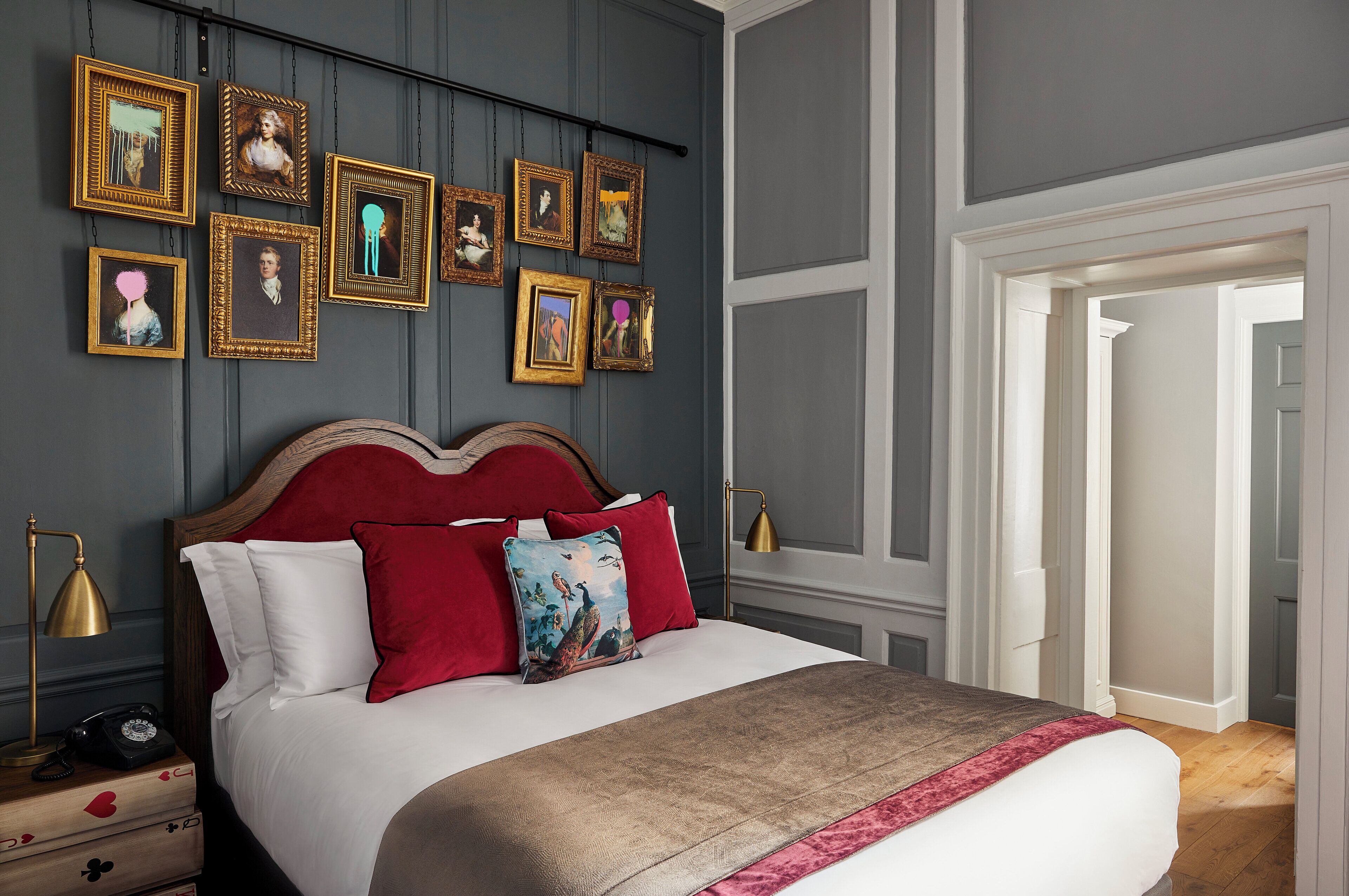 A neatly made bed with red and white pillows, a wooden headboard, and a bedside table with a lamp and a vintage telephone.