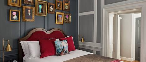 Una cama bien hecha con almohadas rojas y blancas, un cabecero de madera y una mesita de noche con una lámpara y un teléfono antiguo.