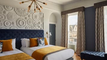 Habitación de hotel con dos camas, un gran muro decorativo, vista a edificios por la ventana y un candelabro.
