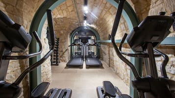A stone-walled gym with treadmills and elliptical machines.