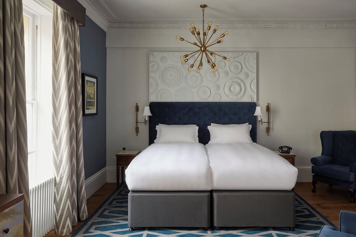 A hotel room with a large bed, a chandelier, a blue upholstered chair, and a patterned wall.