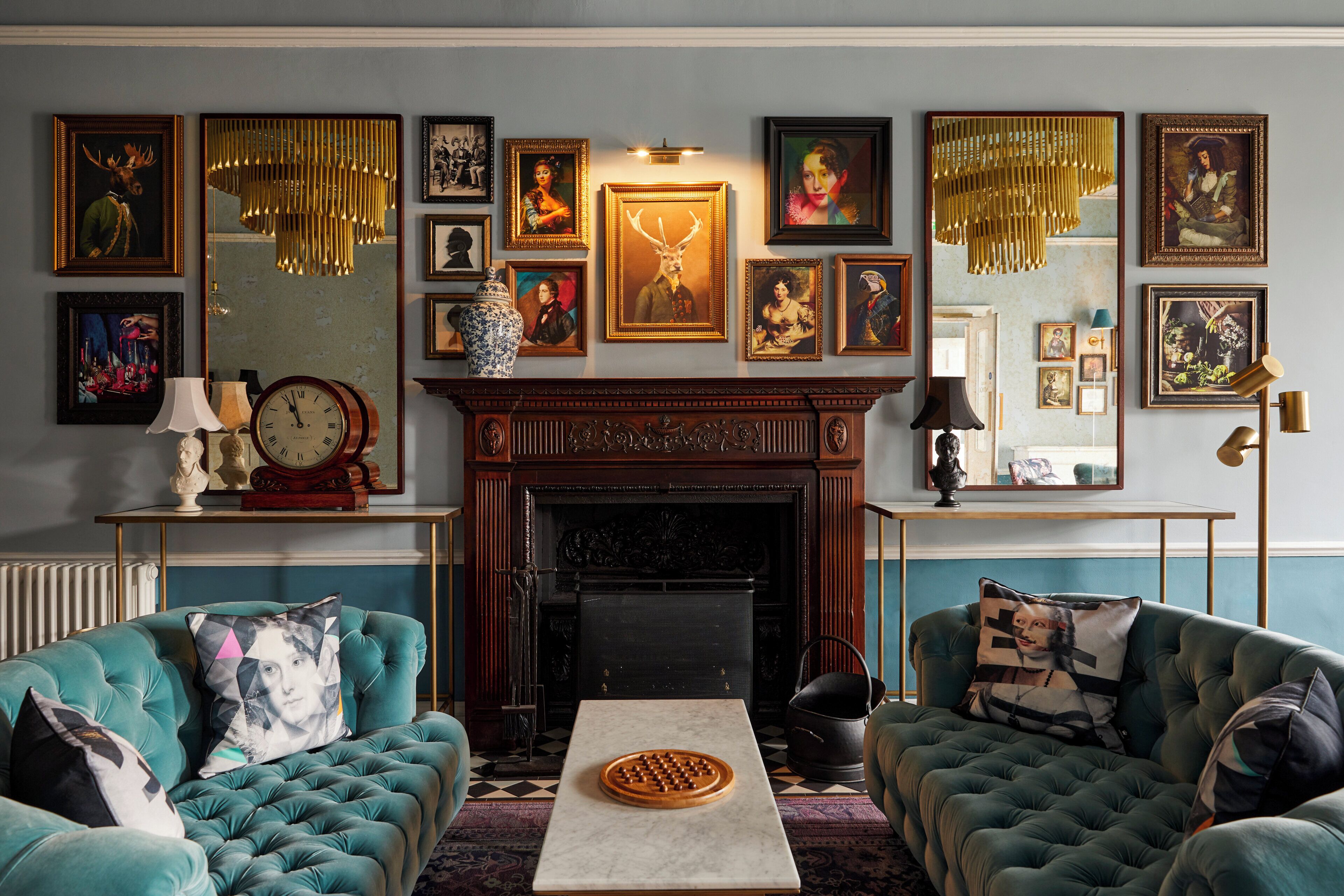 A living room with a fireplace, two armchairs, a coffee table, and a variety of framed artworks on the walls.