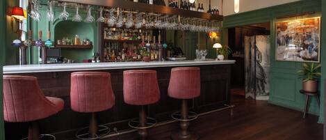 A bar area with a long counter, multiple stools, and a variety of bottles and glasses.