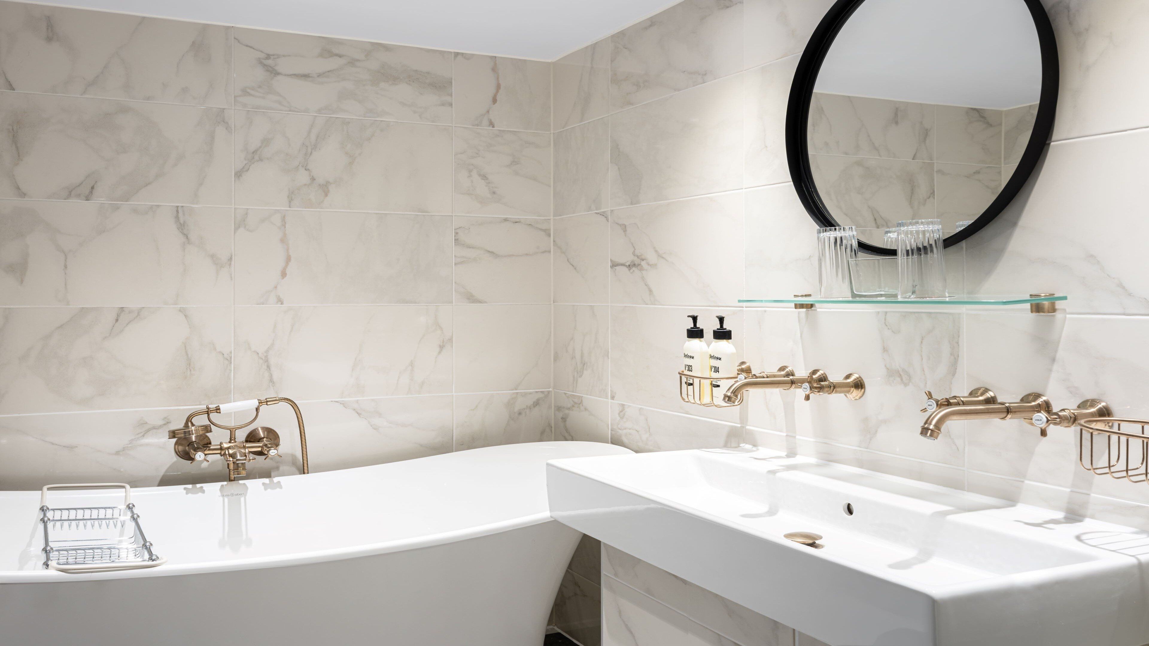 A modern bathroom with a freestanding bathtub, a large mirror, and a glass shelf with toiletries.
