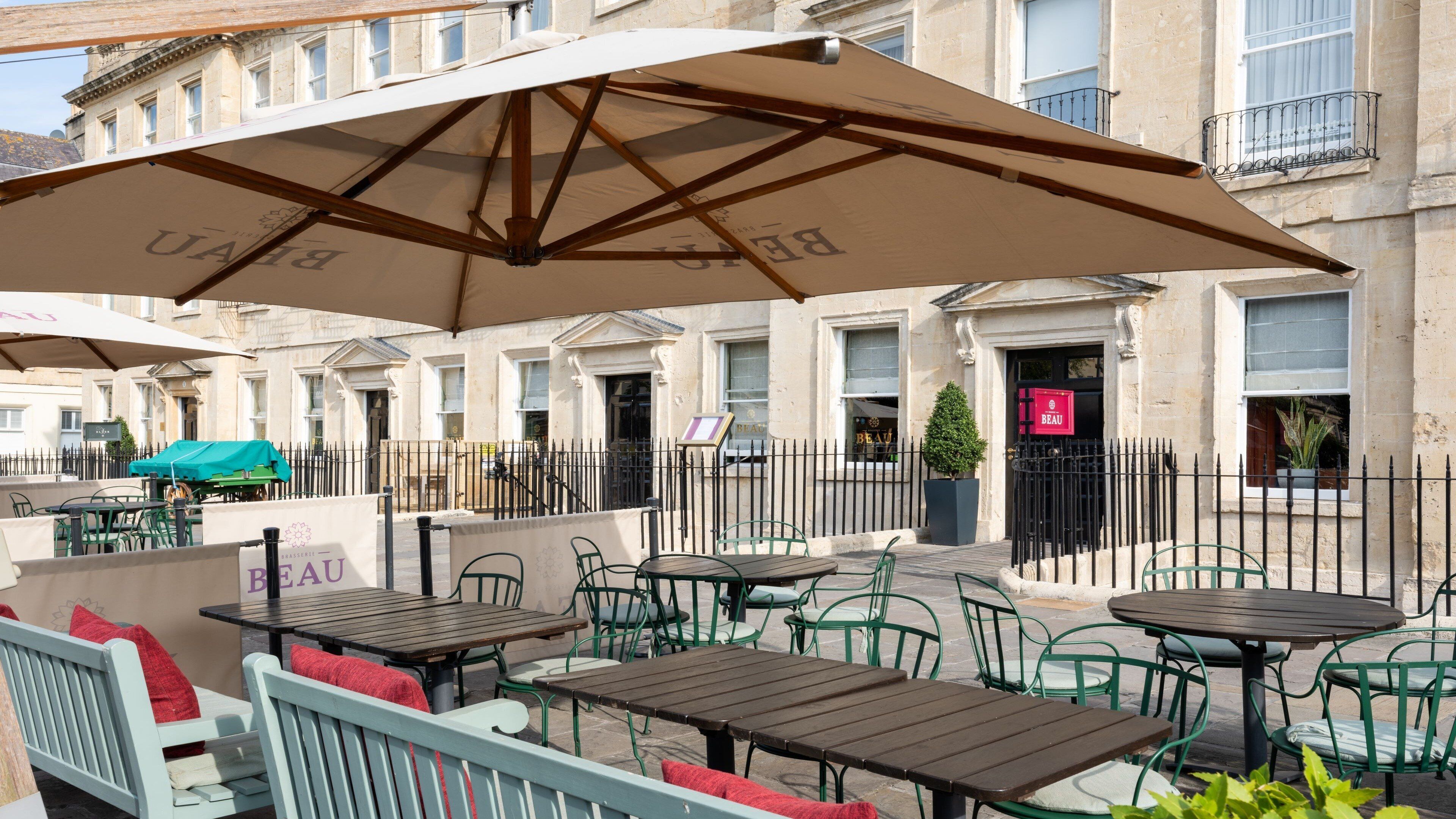 Outdoor seating with tables and chairs, umbrellas, and a building with a sign that reads "BEAU".