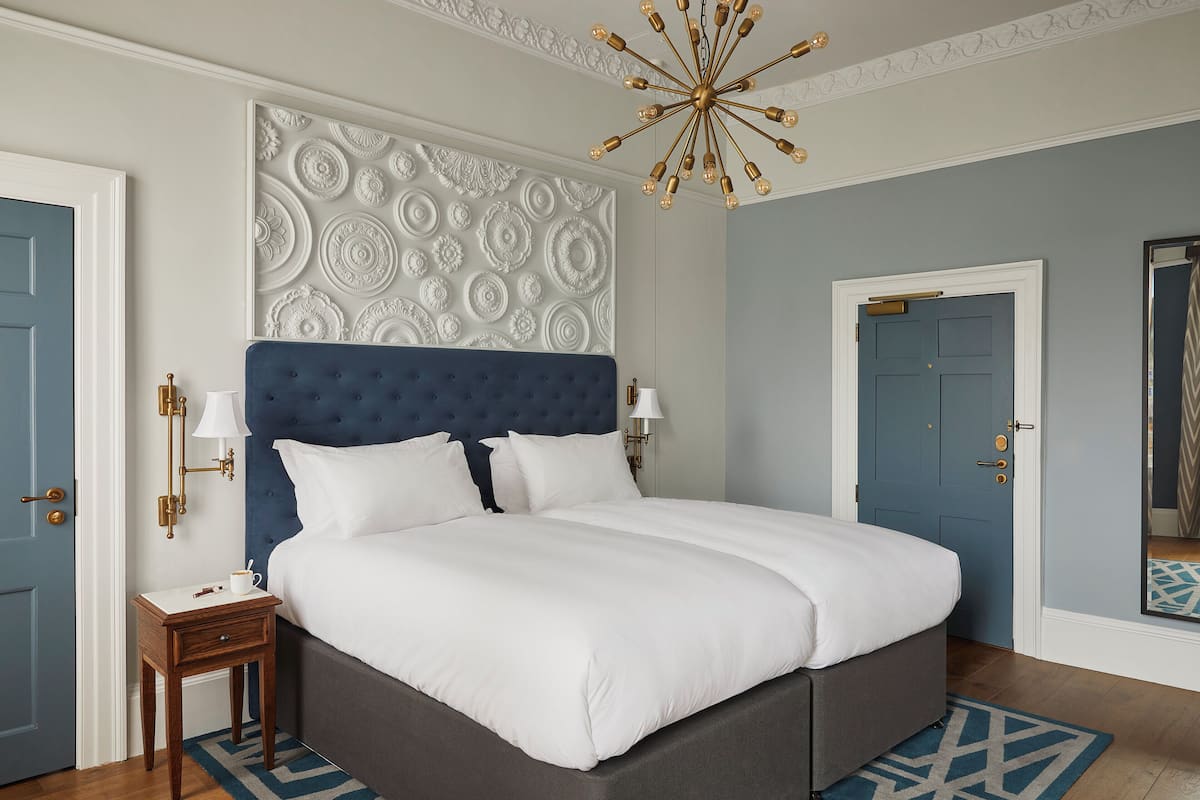 A bedroom with a large bed, a decorative wall panel, a chandelier, and a blue door.