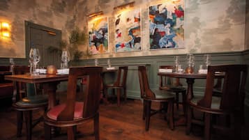 A restaurant interior with wooden tables and chairs, a green wall, and abstract paintings.