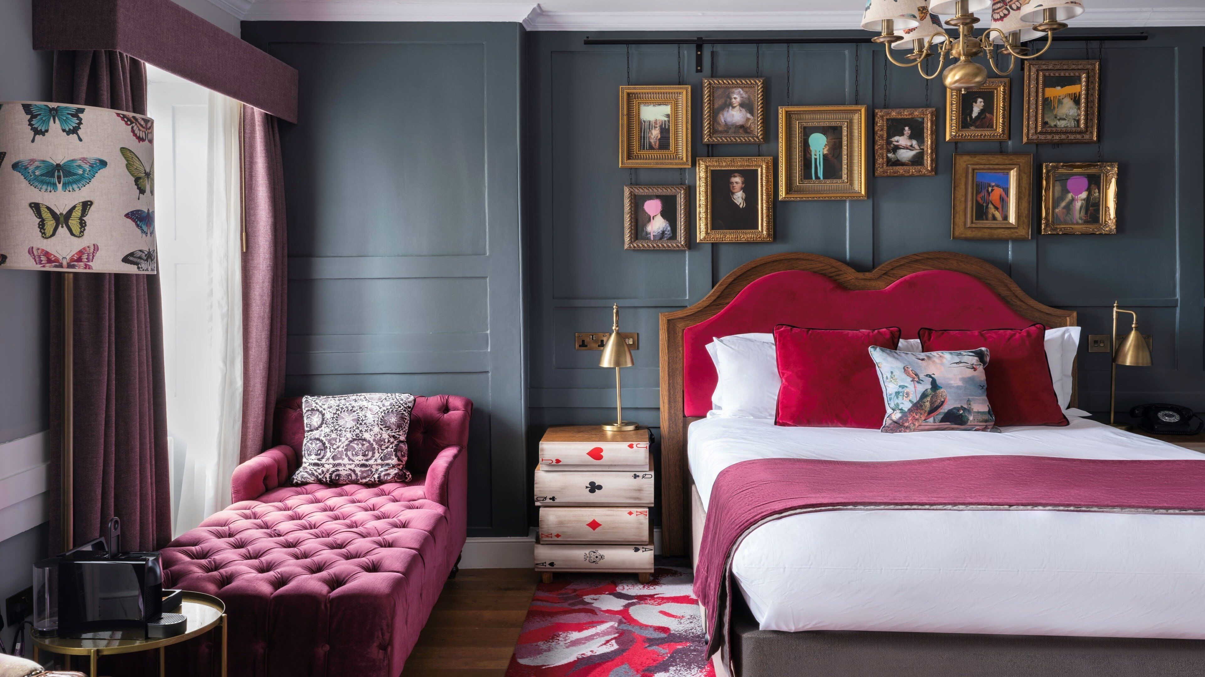 A hotel room with a large bed, a red upholstered chair, a wooden nightstand, and a wall adorned with framed pictures.