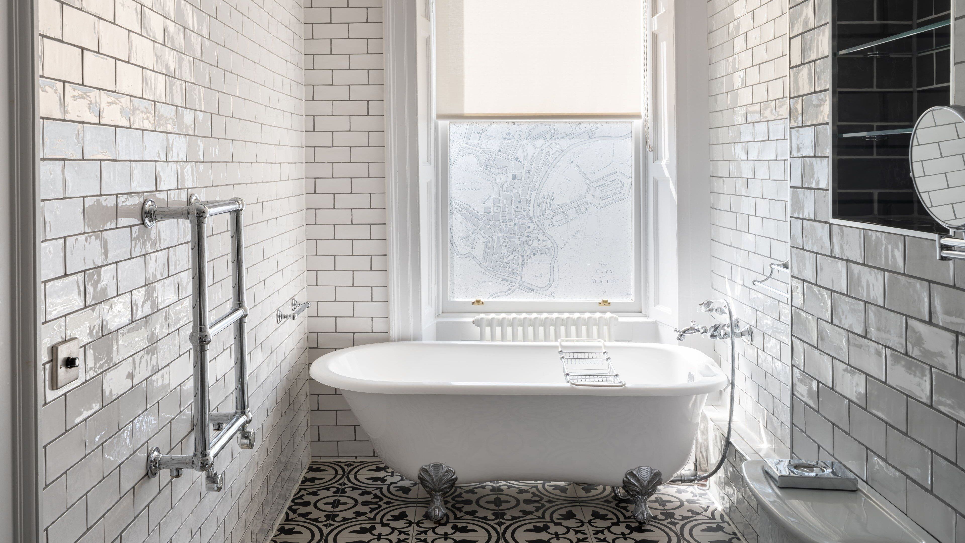 A bathroom with a freestanding bathtub, white tiled walls, a window with a view of a tree, and a radiator.