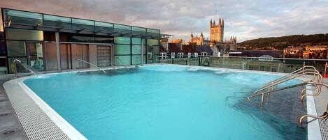 A rooftop pool with a glass enclosure, a view of a historic building, and a cityscape in the background.