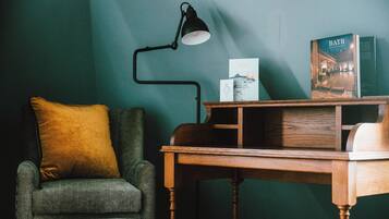 Una habitación con un sillón verde, una mesita de madera, una lámpara de escritorio negra y un libro titulado “BATH” en la pared.