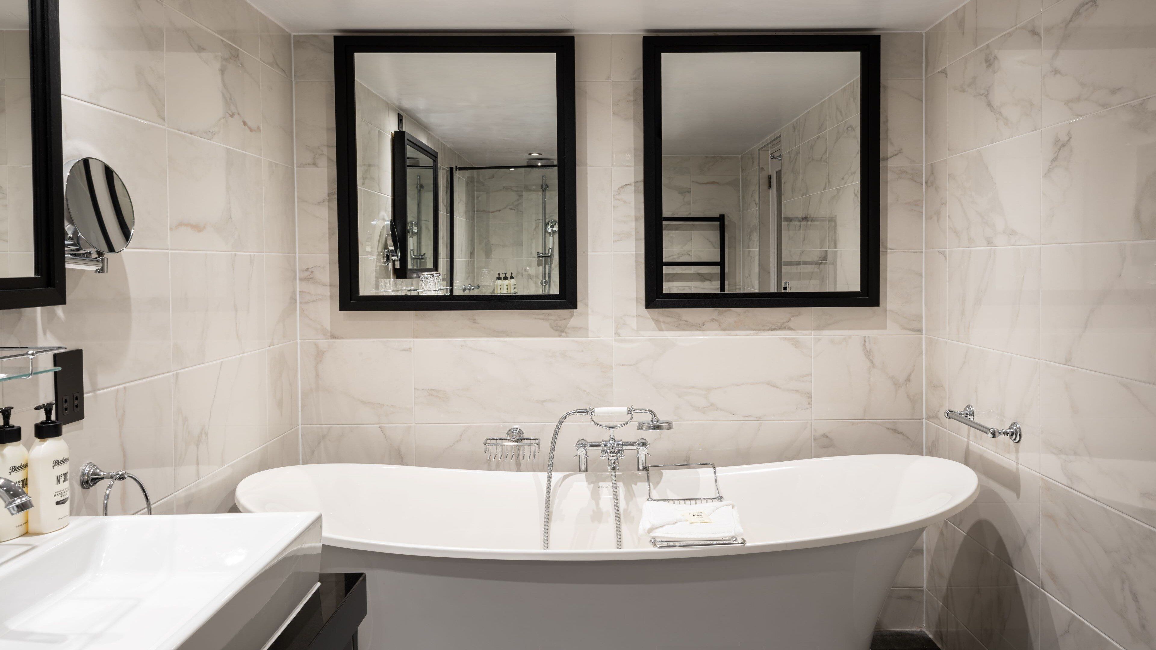 A modern bathroom with a freestanding bathtub, two wall-mounted mirrors, and a glass shelf with toiletries.