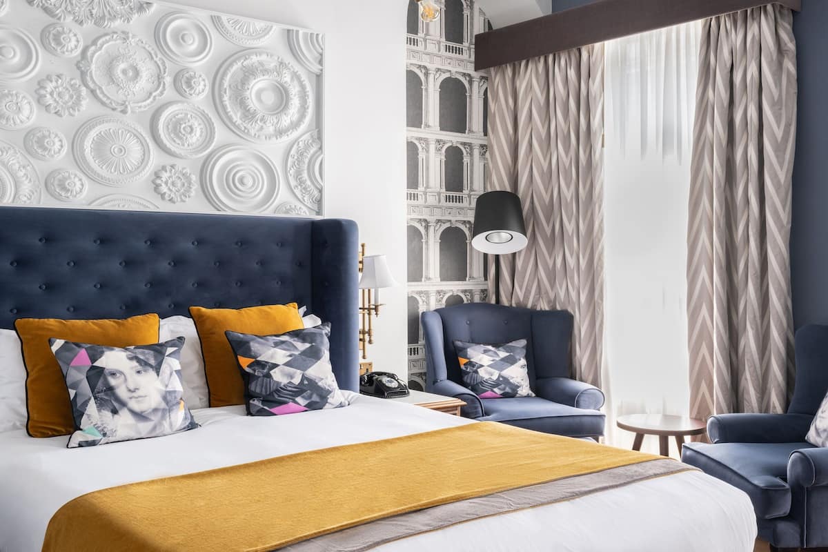 A hotel room with a large bed, two armchairs, a nightstand, and a lamp.