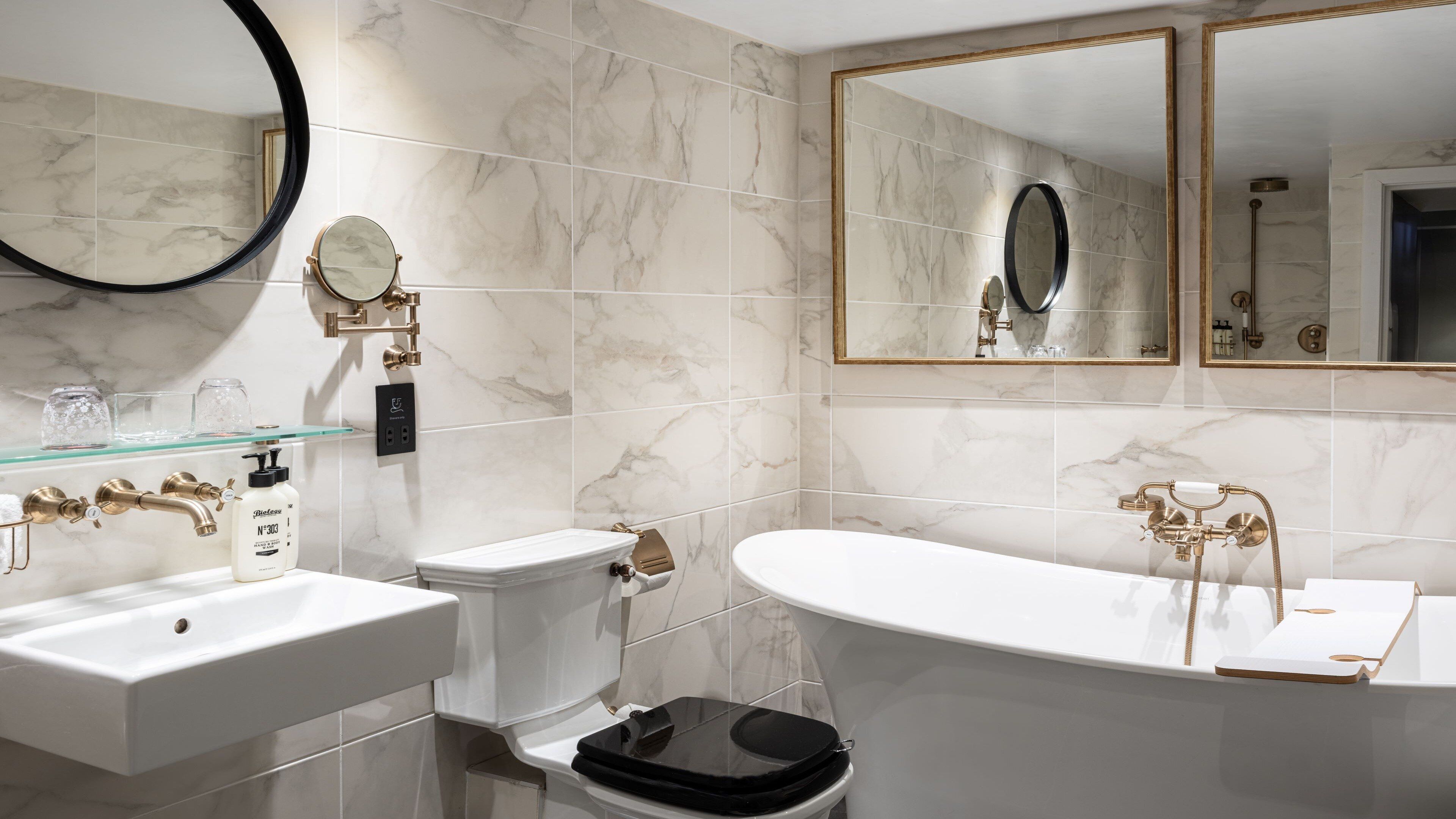 Un baño con lavamanos blanco, inodoro y bañera con detalles dorados.
