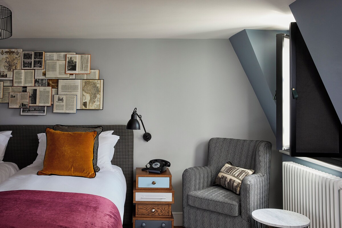 Ein Schlafzimmer mit Bett, Nachttisch, Stuhl, einem an der Wand befestigten Fernseher und einem Heizkörper.