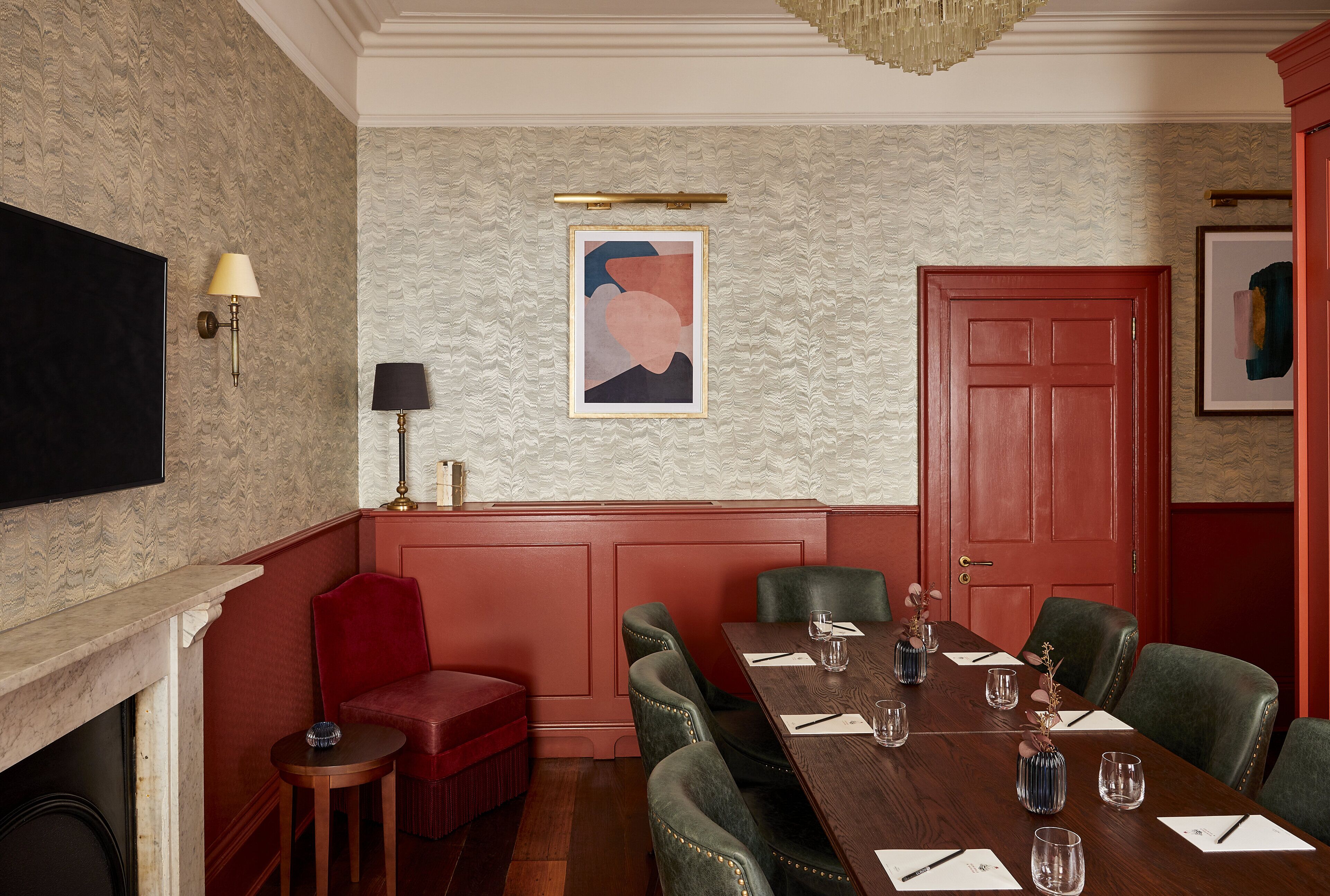 A conference room with a long table, green upholstered chairs, a red door, and a fireplace.