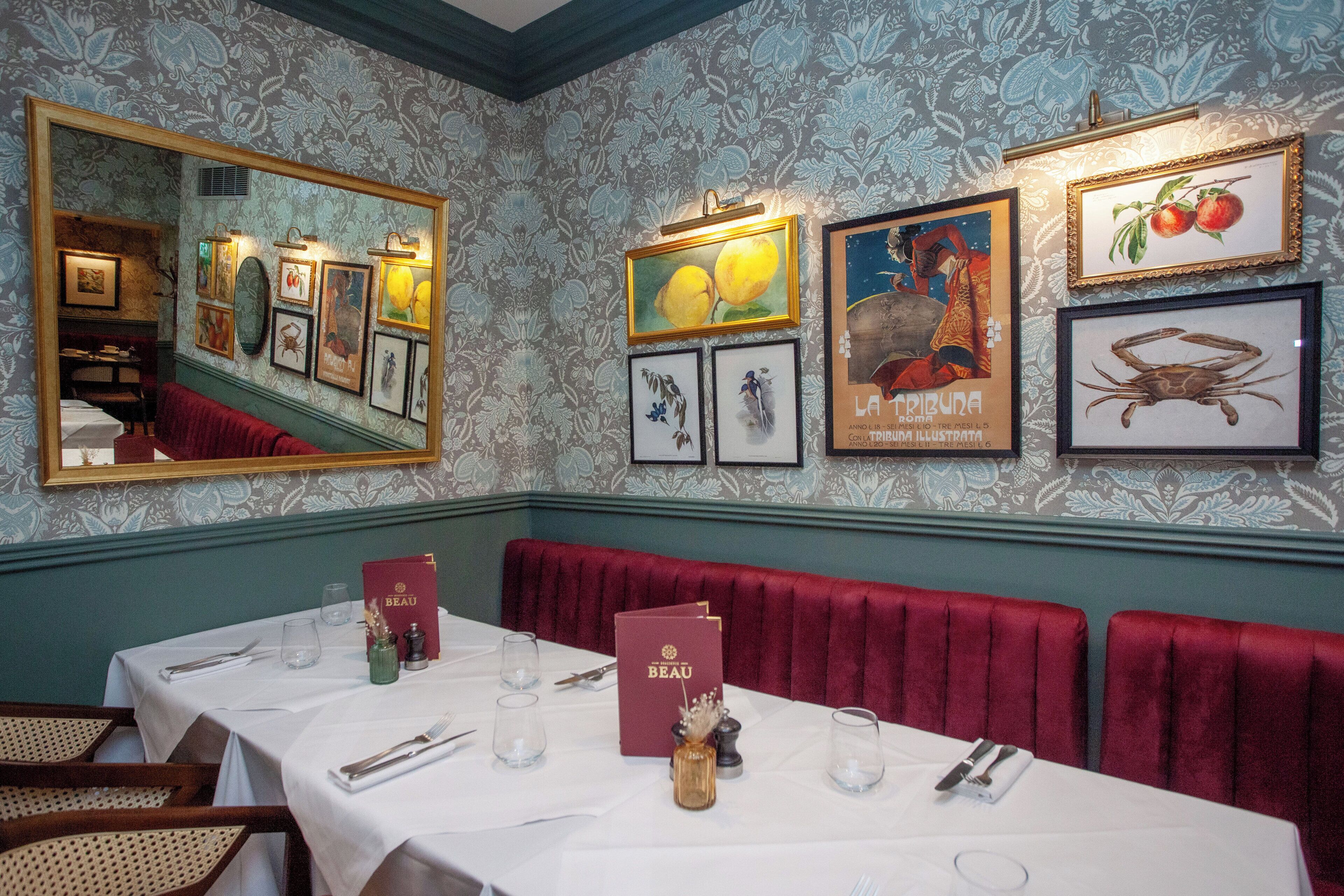 A dining area with a table set for two, framed artwork on the wall, and a red upholstered bench.