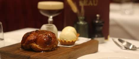 A wooden board with a glazed meat dish and a scoop of ice cream on a table.