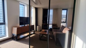 A modern hotel room with large windows, a flat-screen TV, a sofa, a coffee table, and a small table with a lamp. - Ramada Encore by Wyndham Haeundae (Busan)