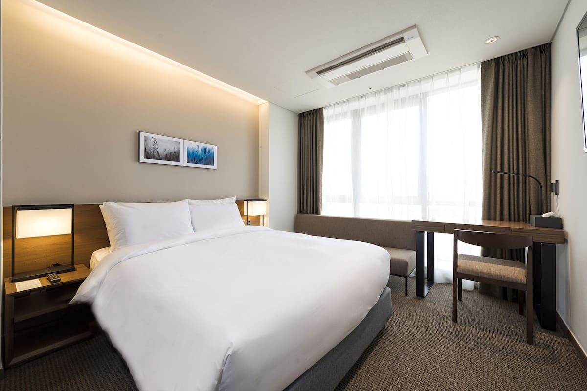 A hotel room with a large bed, bedside tables, a desk, and a chair.