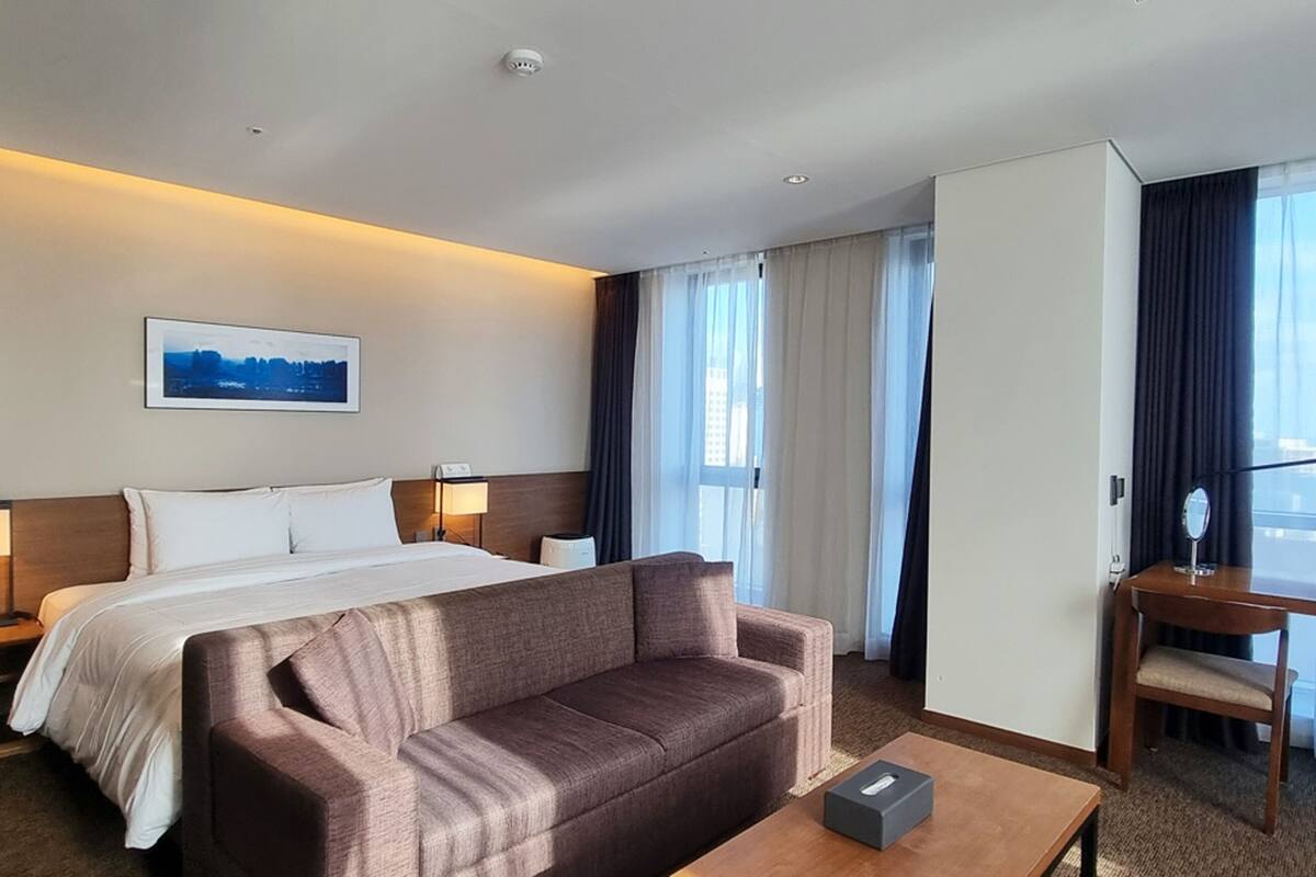 A hotel room with a bed, a sofa, a desk, and a chair.