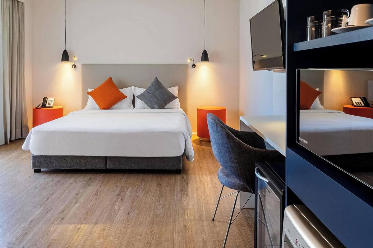 Ein modernes Hotelzimmer mit einem großen Bett, Nachttischen, einem Schreibtisch und einem Fernseher.