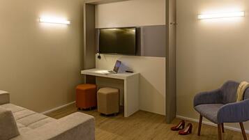 Una habitación compacta con un escritorio, una silla, un sofá y un televisor montado en la pared.