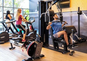 Et fitnesscenter med træningsmaskiner, styrkeløftudstyr og et stort vindue.