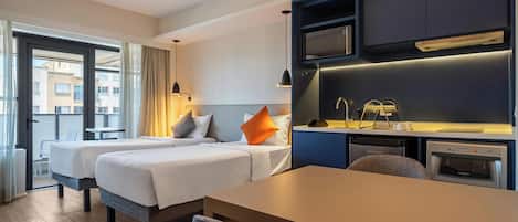 A hotel room with two beds, a dining table, a kitchenette, and a view of the city.