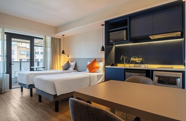 Une chambre d’hôtel avec deux lits, une table à manger, un coin cuisine et une vue sur la ville.