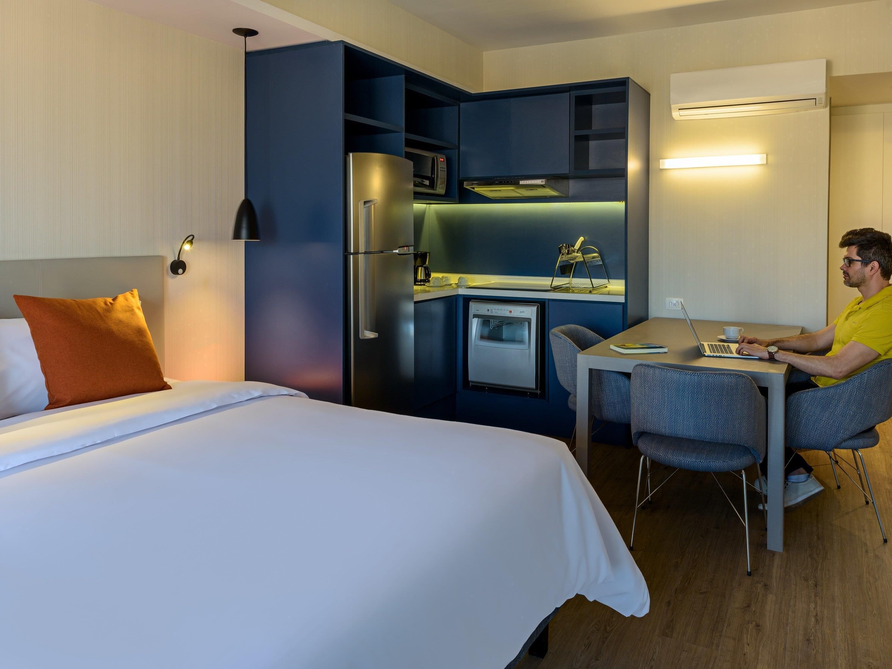 Habitació d'hotel senzilla amb llit, escriptori, petita cuina i microones.