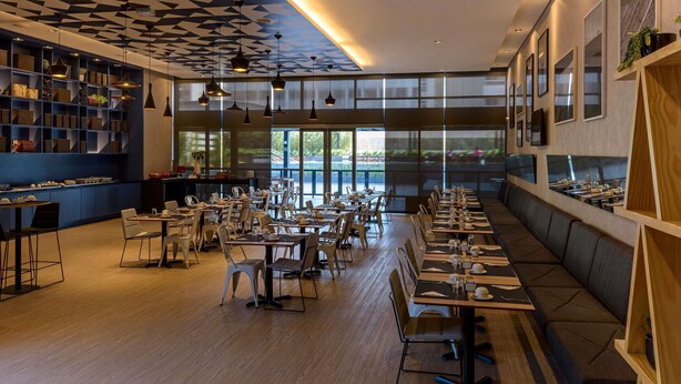 Ein modernes Restaurant mit einem langen Essbereich, hohen Decken und einem geometrischen Deckenmuster.
