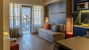 Ein modernes Hotelzimmer mit Sofa, Esstisch, Blick auf die Stadt und einer eingebauten Mikrowelle.