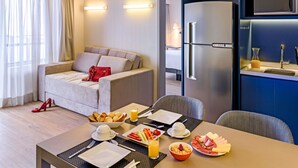 Ein Hotelzimmer mit Essbereich, einer Couch, einem Kühlschrank und Blick ins Freie.