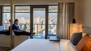 Ein Hotelzimmer mit einem Bett, einem Laptop auf einer Fensterbank und Blick auf die Stadt.