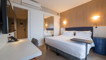 Een hotelkamer met een bed, een bureau, een stoel, een spiegel en een wandairconditioner.