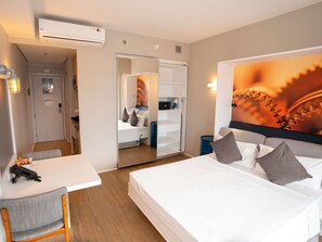 Une chambre d’hôtel comprenant un lit, un bureau, une chaise, une armoire et un grand miroir.