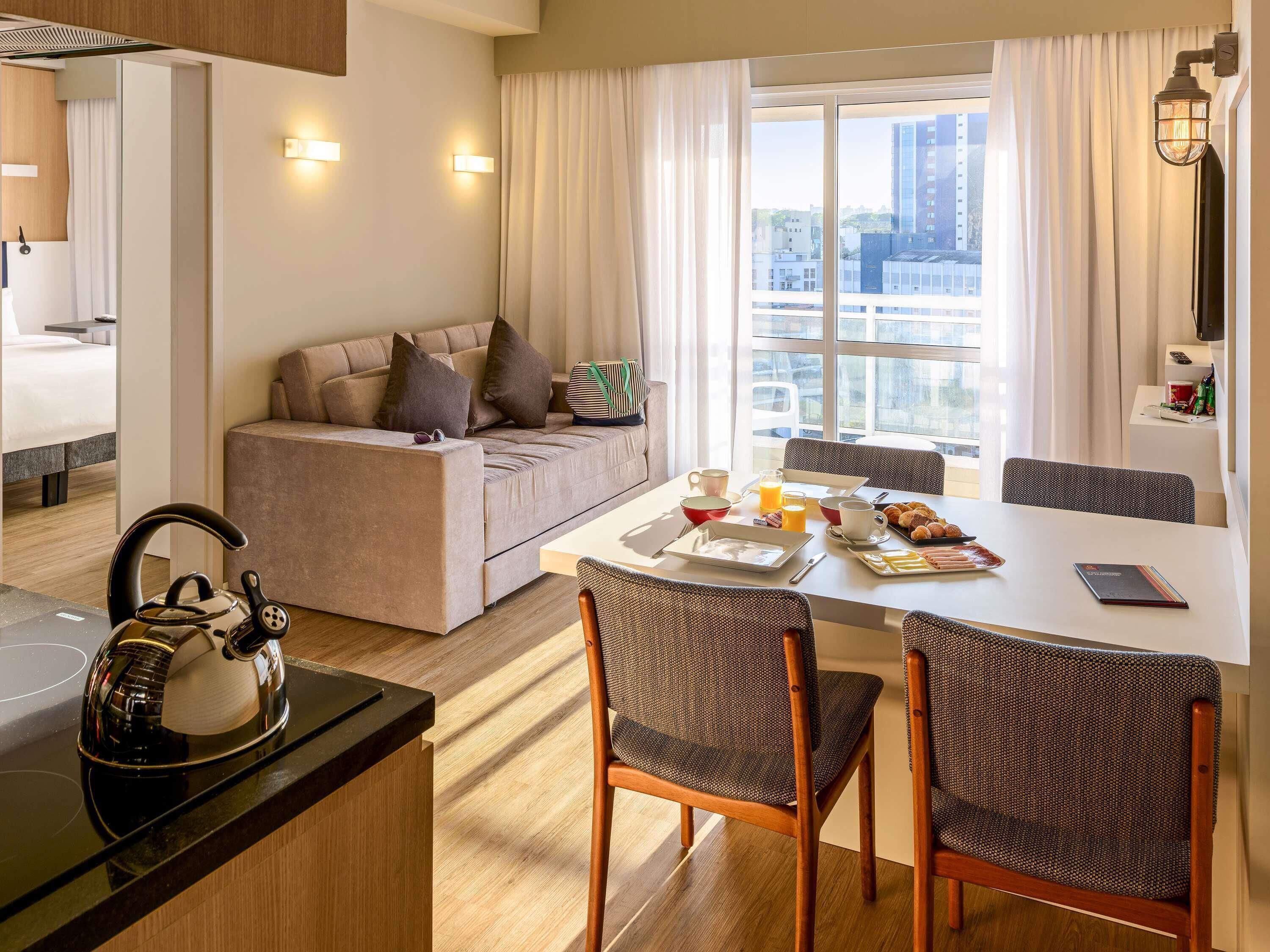 Une chambre d’hôtel moderne dotée d’un coin repas, d’un canapé et offrant une vue sur la ville.
