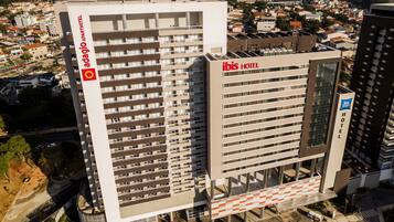 A high-rise hotel with multiple floors, a prominent "ibis hotel" sign, and a large parking structure below.