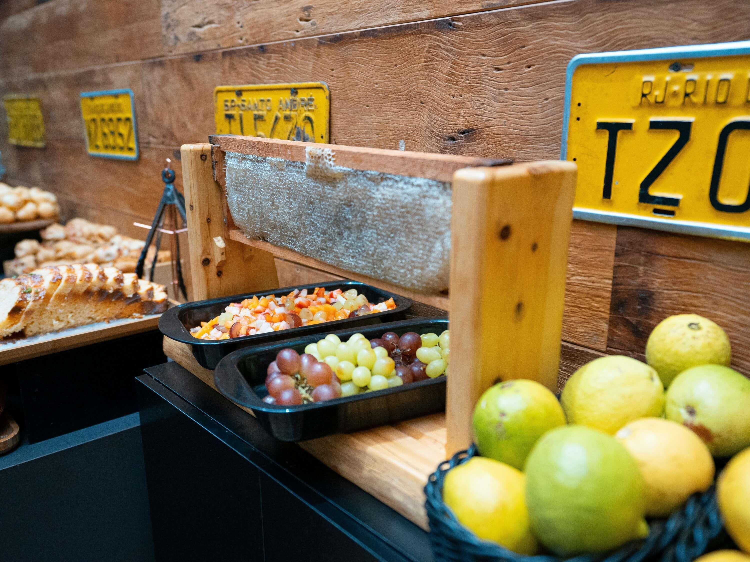 Un bufé con diversos alimentos, que incluye un rallador de madera, una bandeja de frutas mixtas y una cesta de manzanas.