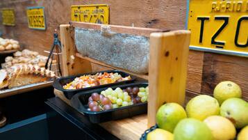 Un bufé con diversos alimentos, que incluye un rallador de madera, una bandeja de frutas mixtas y una cesta de manzanas.