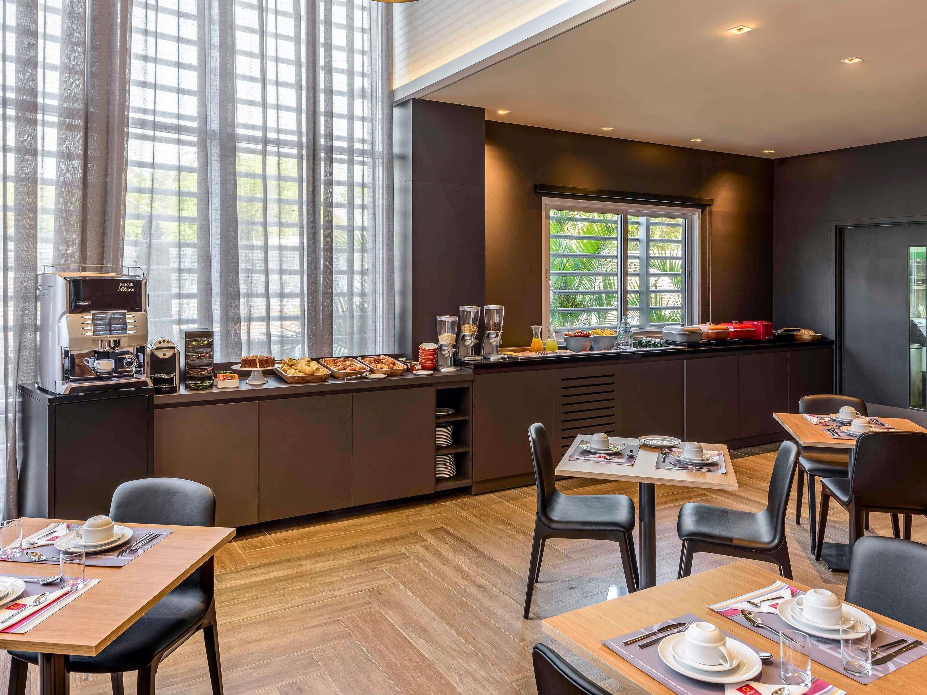 A modern dining area with a coffee station, tables set for dining, and large windows providing natural light.