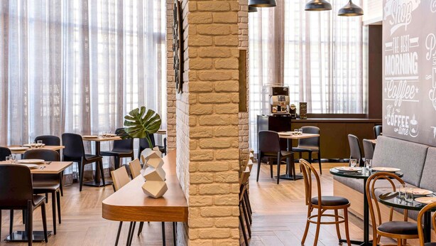 Een modern café met zichtbare bakstenen muren, hanglampen en een mix van houten en gestoffeerde zitplaatsen.