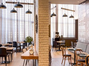 Un café moderne avec des murs en briques apparentes, des luminaires suspendus et un mélange de sièges en bois et de sièges rembourrés.