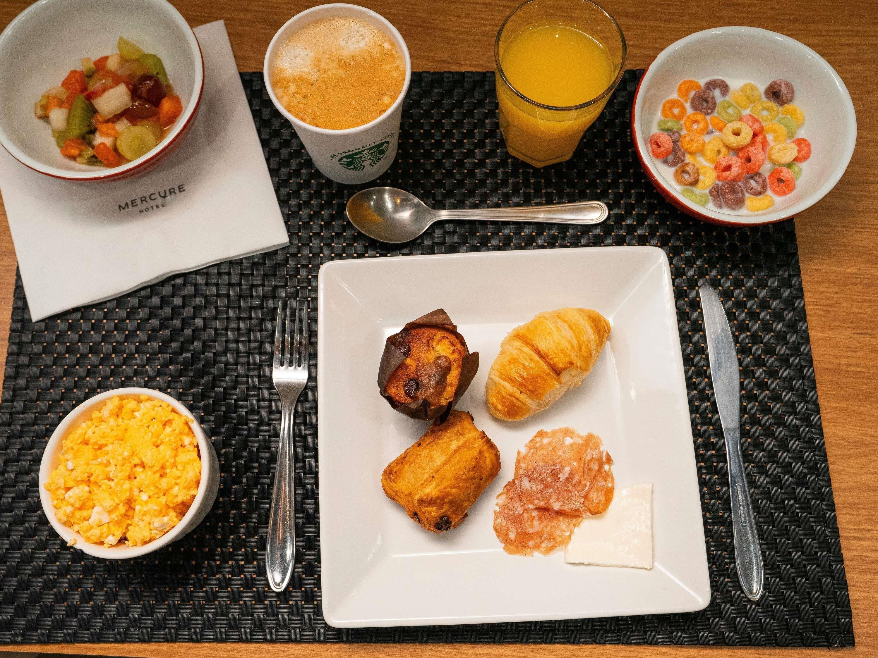 Un desayuno con cruasanes, huevos revueltos y un bol de fruta.