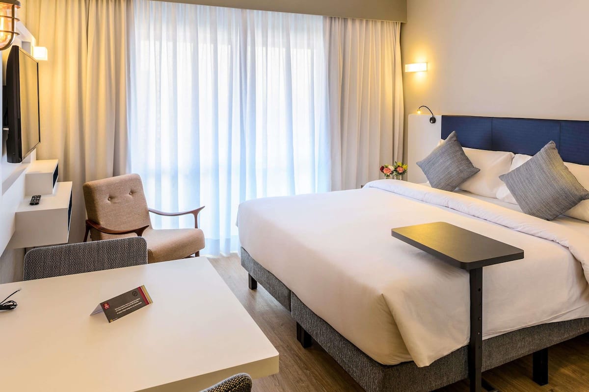A hotel room with a bed, a desk, a chair, a TV, and a window with curtains.
