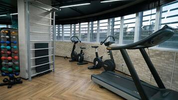 Un gimnasio con equipo de ejercicio, piso de madera y ventanas amplias.