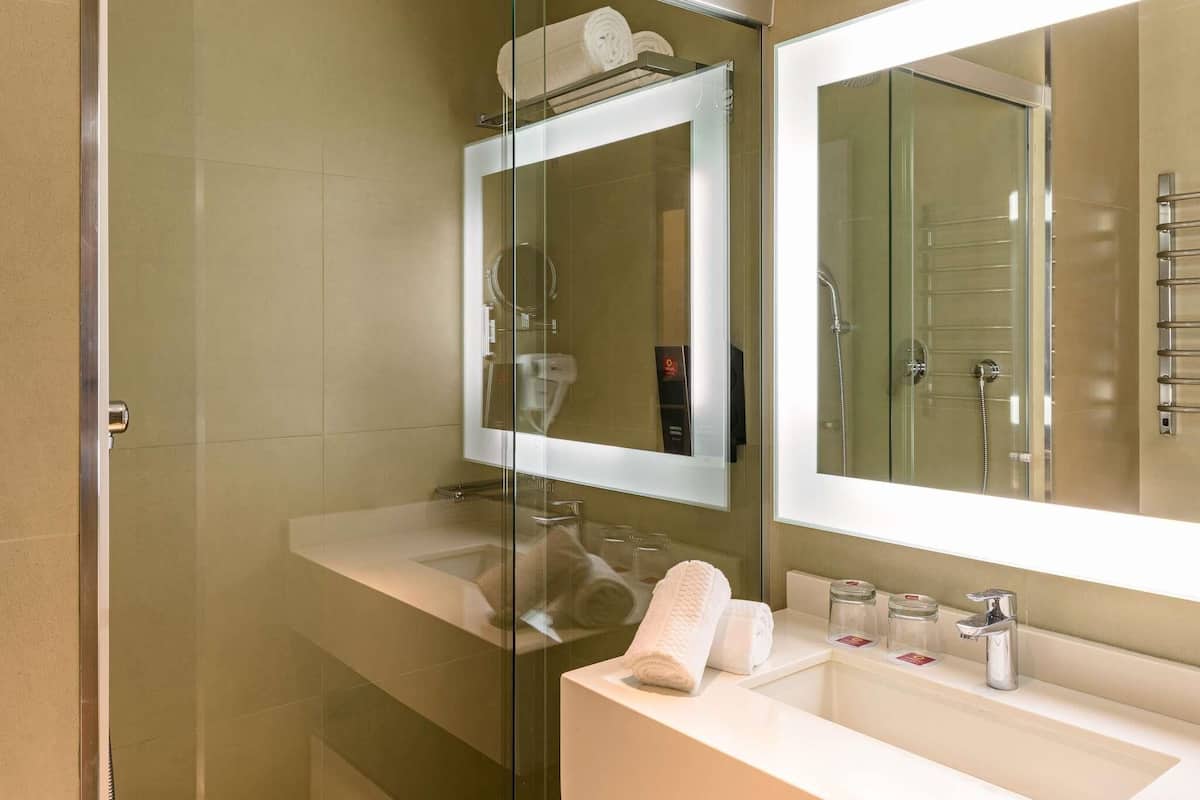 Un bany modern amb plat de dutxa envoltat de vidre, un mirall gran i un lavabo blanc.